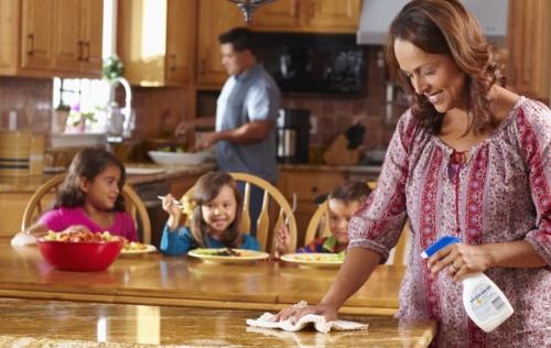 Mother cleaning while children eat in background
