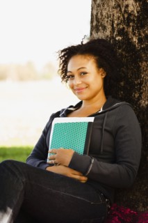 African woman holding book leaning against tree
