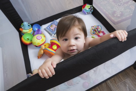 Mixed race baby girl standing in playpen