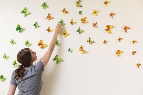 Mixed race woman decorating wall with butterflies