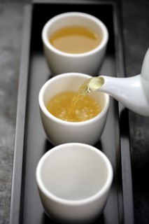 Green tea being poured from teapot into cups on tray