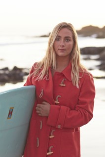 Caucasian woman in coat carrying surfboard on beach