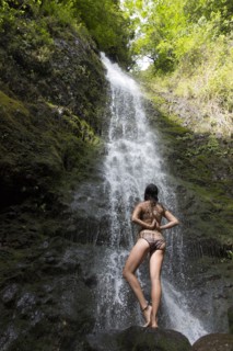 Caucasian woman standing on rock near waterfall performing yoga