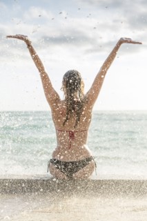 Ocean waves splashing on Caucasian woman wearing bikini
