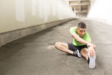 Mixed Race man sitting on ground stretching leg