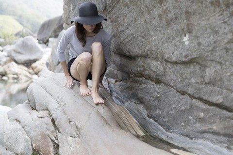 Woman wearing sun hat crouching on rock