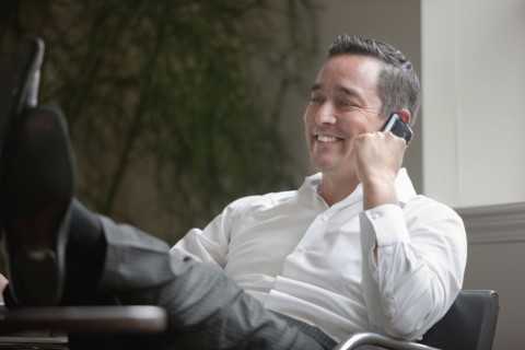Mixed race businessman with feet on desk using cell phone