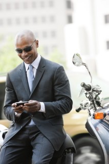 Black businessman sitting on scooter text messaging