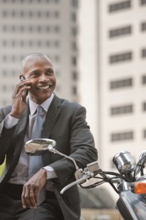 Black businessman sitting on scooter talking on cell phone