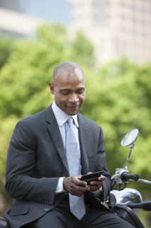 Black businessman sitting on scooter text messaging