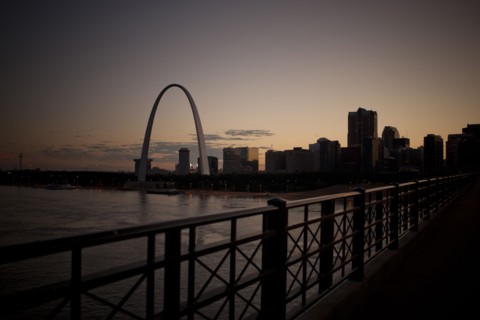 Arch landmark next to urban river at sunset