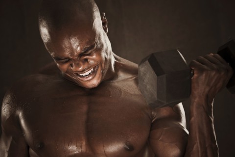 Grimacing African American man lifting weights