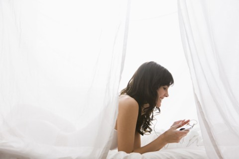 Caucasian woman laying in bed listening to mp3 player