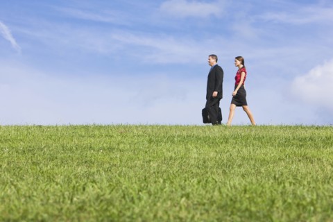 Caucasian co-workers walking through grassy field
