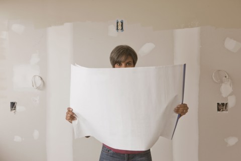 Mixed race woman standing in unfinished room with blueprints