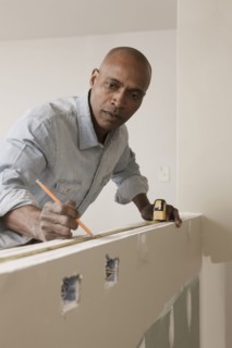 African American man measuring wall in unfinished room
