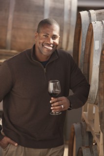 Black man drinking wine near wine barrel