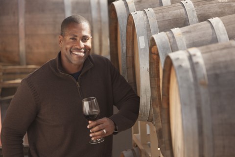 Black man drinking wine near wine barrel