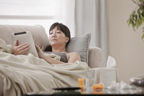 Sick Asian woman using digital tablet on sofa