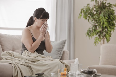 Sick Asian woman sitting on sofa blowing her nose
