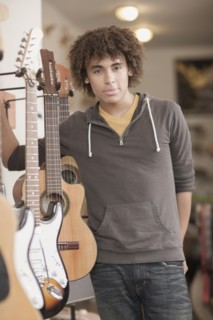 Mixed race teenager standing with guitars in music store