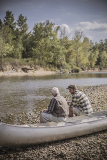 Caucasian father and son sitting in canoe on riverbed