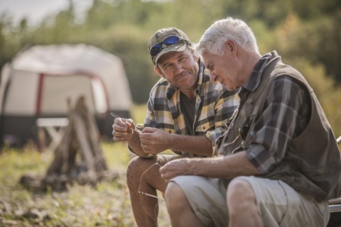 Caucasian father and son tying fishing lures at campsite