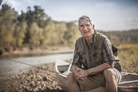 Older Caucasian man holding fishing rod near river
