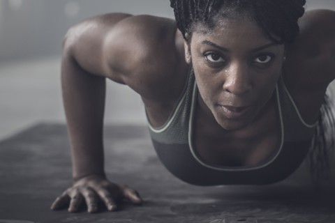 Black woman doing push-ups in dark gym