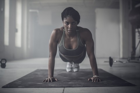 Black woman doing push-ups in dark gym