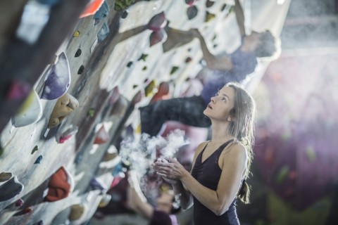 Athlete chalking her hands at rock wall in gym