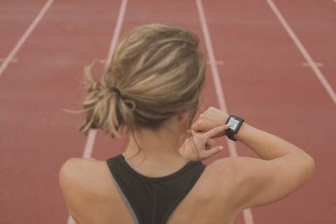 Caucasian runner checking watch on sports field