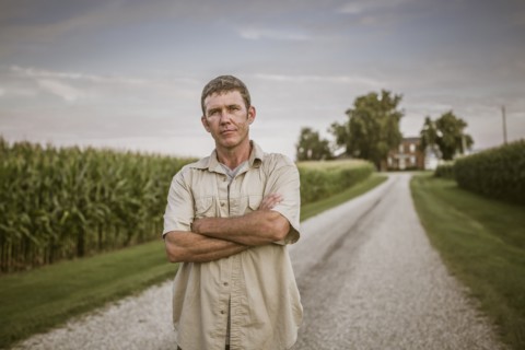Caucasian farmer standing on dirt road by corn field