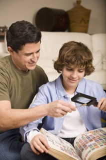 Hispanic father and son examining stamp through magnifying glass
