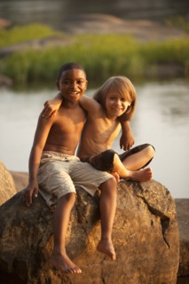 Smiling boys hugging on rock near lake