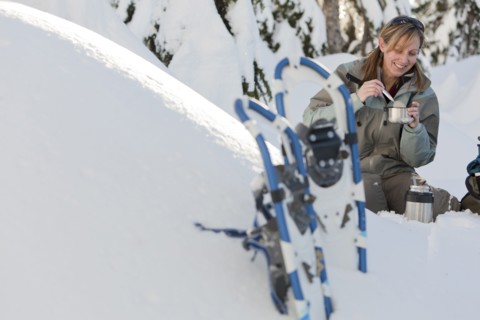 Caucasian woman with snowshoes eating in snow