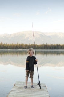 Caucasian boy standing on dock at lake holding fishing rod