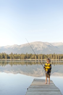 Caucasian boy standing on dock at lake holding fishing rod