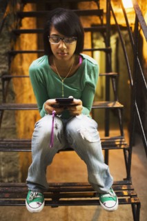 Hispanic girl text messaging on staircase