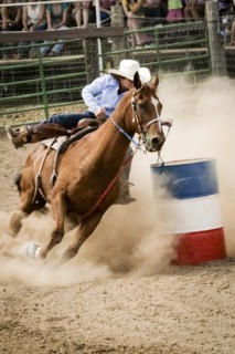 Cowgirl riding horse near barrel in rodeo