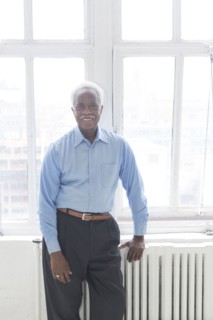 Smiling older Black man leaning on radiator near window