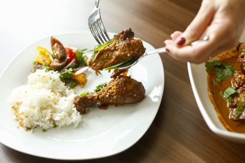 Woman holding meat over plate with fork and spoon