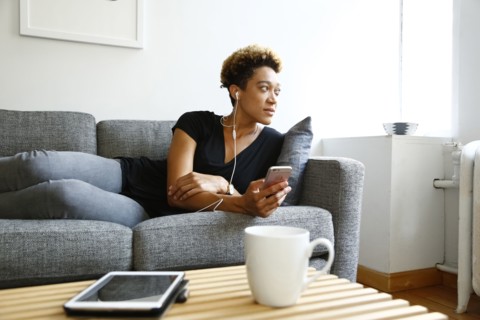 Mixed race woman laying on sofa listening to earbuds
