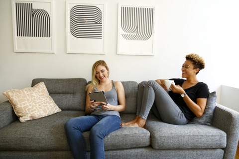Women drinking coffee and using digital tablet on sofa