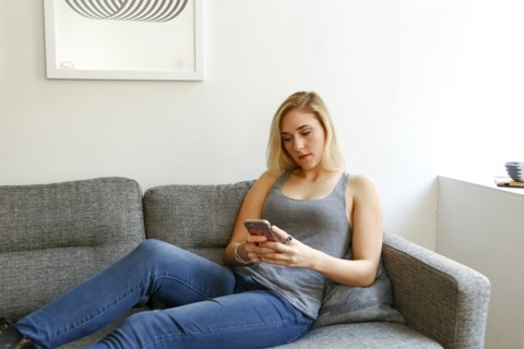 Caucasian woman sitting on sofa texting on cell phone