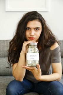 Portrait of mixed race woman holding jar of money for student loan