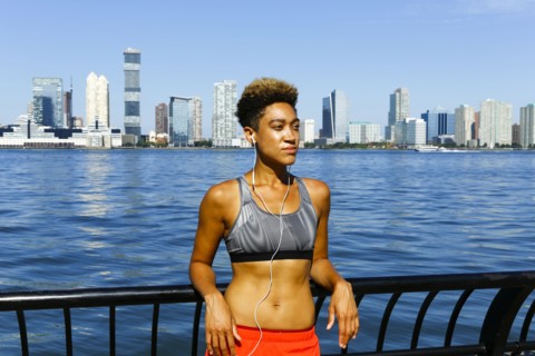 Mixed race woman leaning on railing at waterfront listening to earbuds