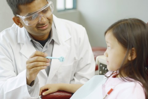 Indian male dentist with Asian girl in dentist's chair