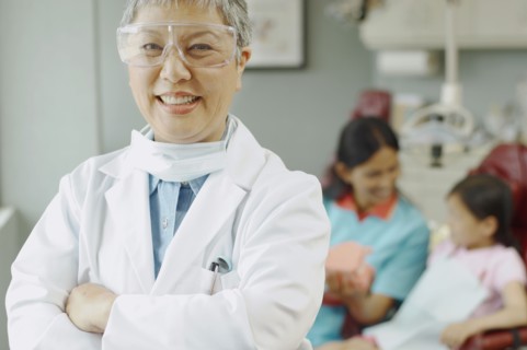 Senior Asian female dentist with assistant and patient in background