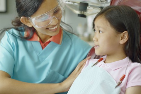 Indian female dental assistant smiling at young Asian female patient